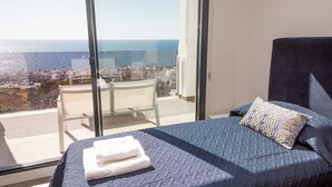 Ein Schlafzimmer mit einem großen Fenster, einem Bett mit blauer Steppdecke, einem weißen Handtuch und einem gemusterten Kopfkissen.