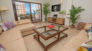 A modern living room with a glass coffee table, beige sofa, and potted plants. - Marina de la Duquesa 1031 (Manilva)