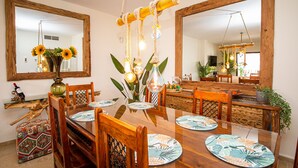 A dining area with a wooden table, chairs, and a large mirror. There are decorative plants and a vase with flowers on the table. - Marina de la Duquesa 1031 (Manilva)