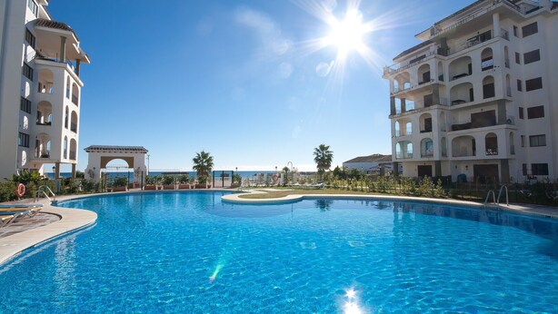 A large swimming pool with a clear view of the ocean, surrounded by multi-story buildings with balconies. - Marina de la Duquesa 1031 (Manilva)