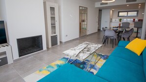 A modern living room with a fireplace, a sofa with a colorful rug, and a dining area with chairs and a table. - Blue Suites apto B5-203 (Manilva)
