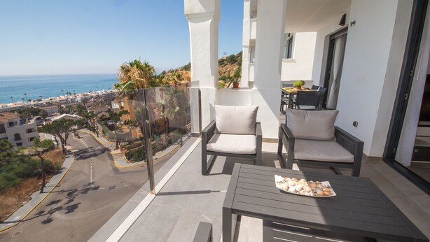 A balcony with two chairs and a table, overlooking a coastal town and the sea. - Blue Suites apto B5-203 (Manilva)
