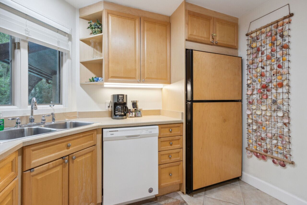 Una cocina con armarios de madera, un lavavajillas blanco, un refrigerador negro y un adorno de conchas marinas en la pared.