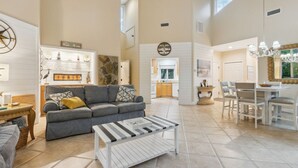 A spacious living area with a gray sofa, a coffee table, and a dining table with chairs. A kitchen is visible in the background. - *NEW* Pool, walk to Beach and 10 hole golf course! (Fernandina Beach)