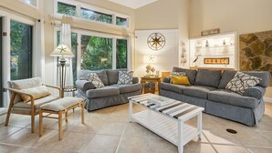A spacious living room with two grey sofas, a wooden chair, a white coffee table, and a large window offering a view of trees. - *NEW* Pool, walk to Beach and 10 hole golf course! (Fernandina Beach)