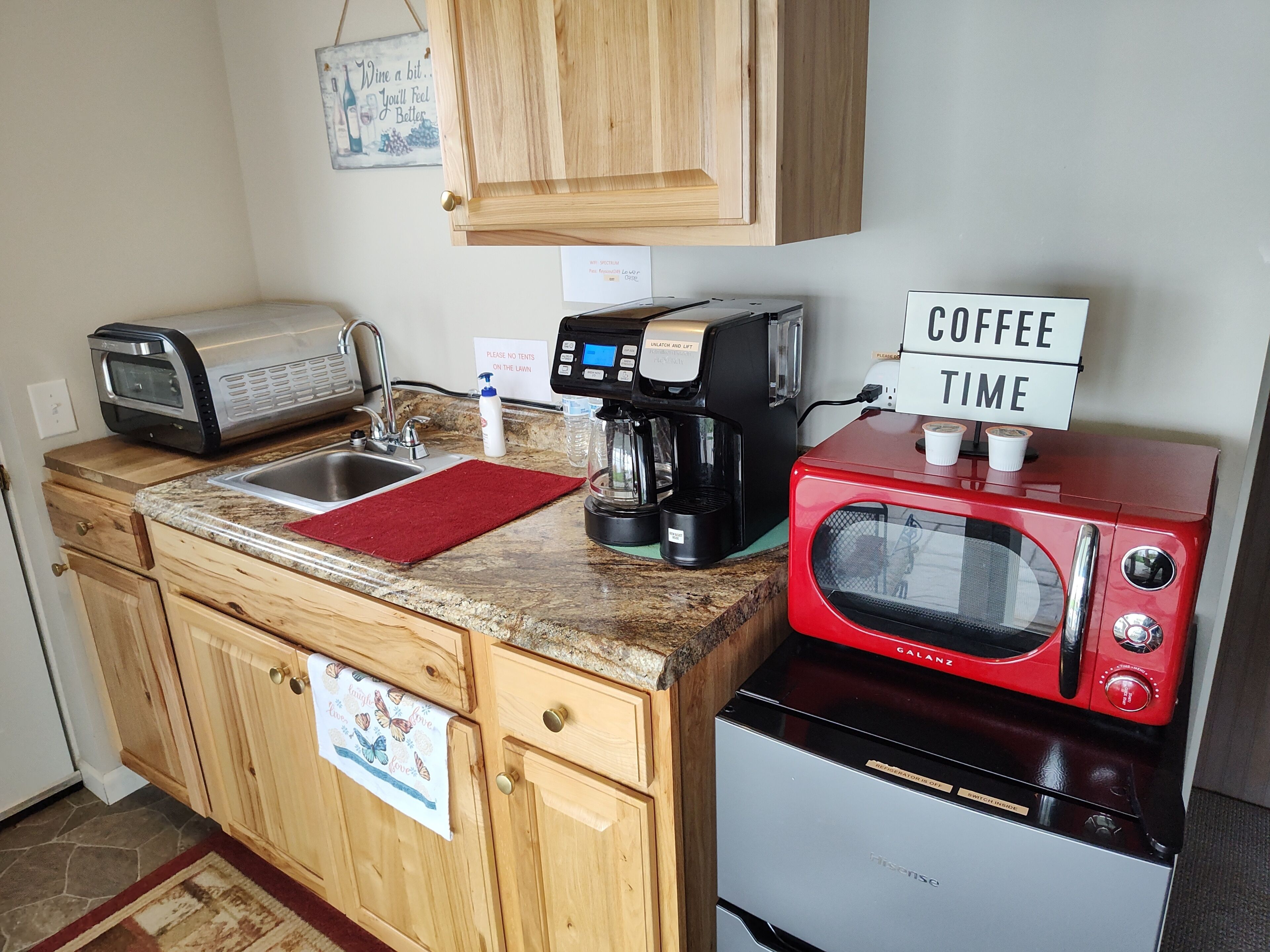A compact kitchen with a sink, a coffee maker, a toaster, a microwave, and a sign that says 'COFFEE TIME'.