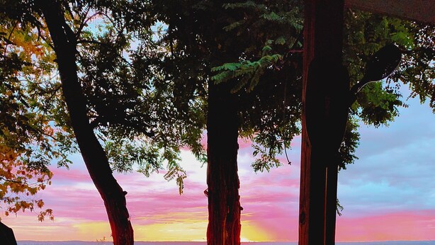 A patio with a table, a bench, and a view of the sunset over the water.