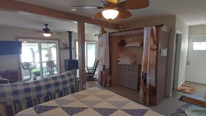 A room with a bed, a chair, a table, a wardrobe, and a ceiling fan.