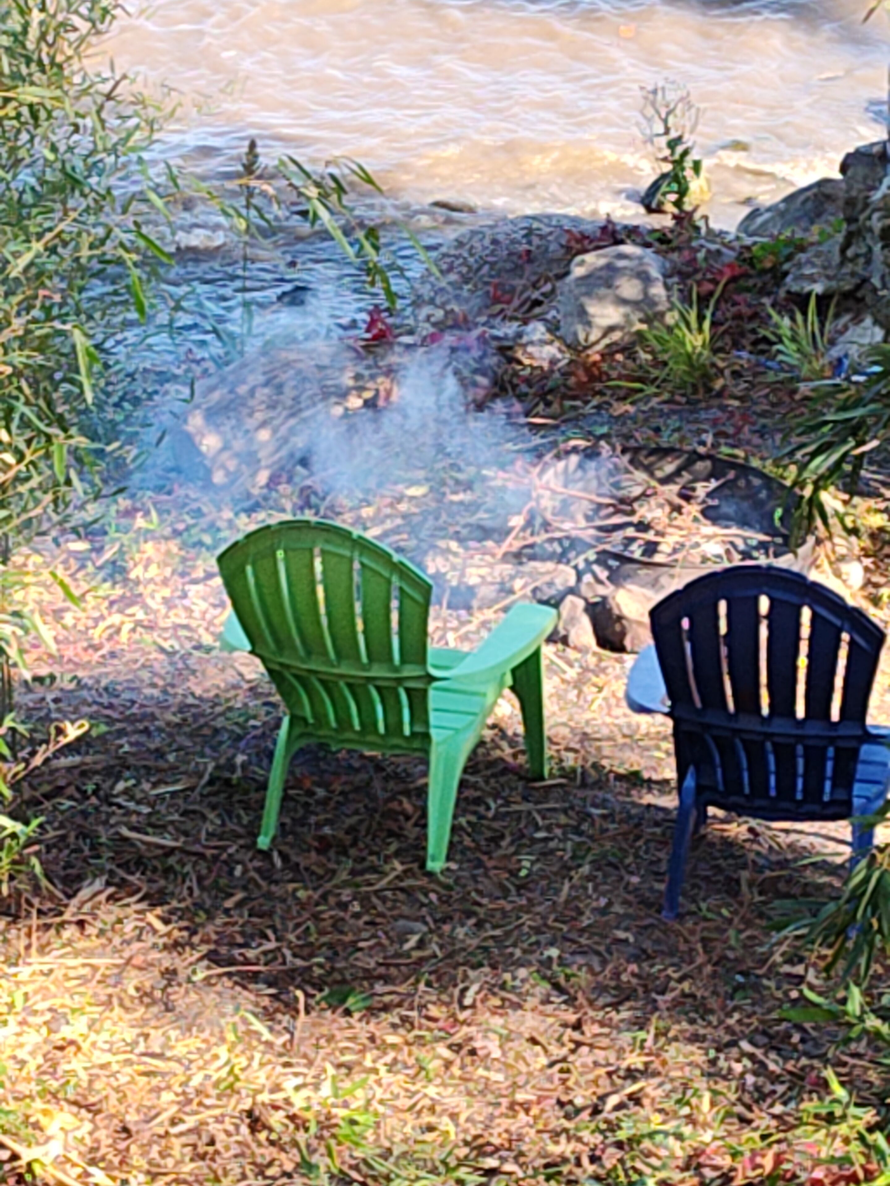 Two chairs by a small body of water with rocks and plants around.