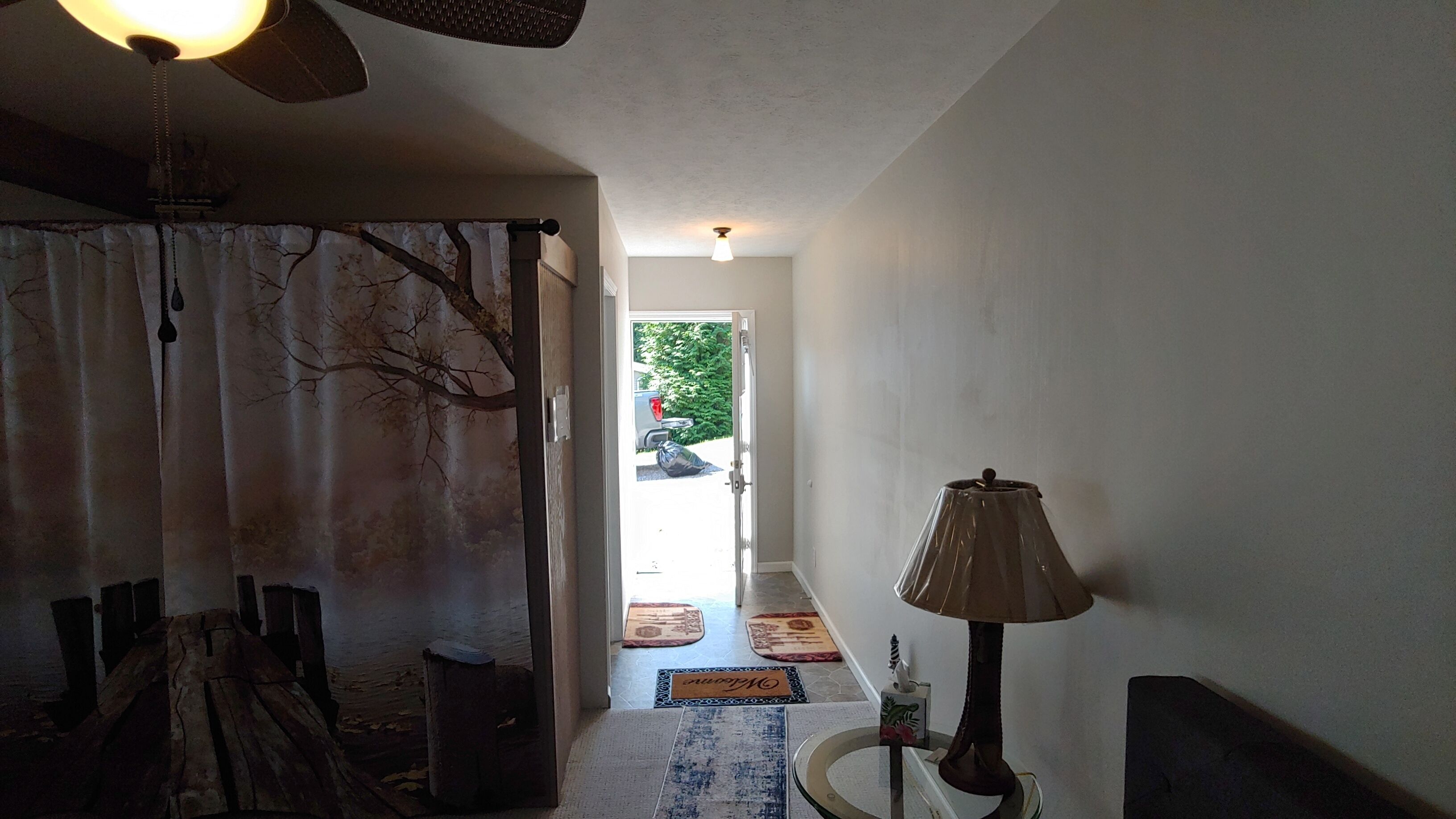 A hallway with a wooden door, a lamp, and a view of a car outside.