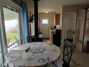 A dining area with a table covered by a nautical-themed tablecloth, a chair, and a view of the backyard through a glass door.
