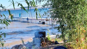 Two chairs near a beach with a view of the sea and a dock in the background.