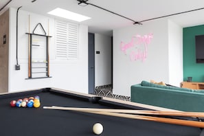 Ein Billardtisch mit Kugeln, ein Neonzeichen, eine Couch und ein Fernseher.