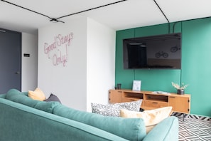 A modern living room with a teal sofa, a mounted TV, and a wall with a motivational quote.