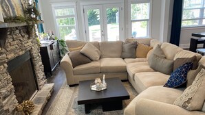 A living room with a stone fireplace, a beige sectional sofa, a coffee table, and a patterned rug. - Gorgeous 3 bedroom house with patio and firepit (Charlotte)