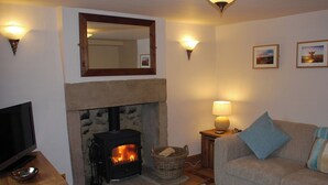 A living room with a stone fireplace, a television on a wooden stand, a sofa with a blue pillow, and two wall-mounted lamps. - 2 bedroom accommodation in Youlgreave near Bakewell (Youlgreave near Bakewell)
