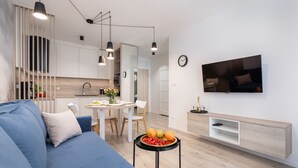 A modern living room with a blue sofa, a dining area with a white table, and a kitchen in the background.