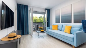 A modern living room with a blue sofa, a small table with a hat and flowers, and a view of the outdoors through a glass door.