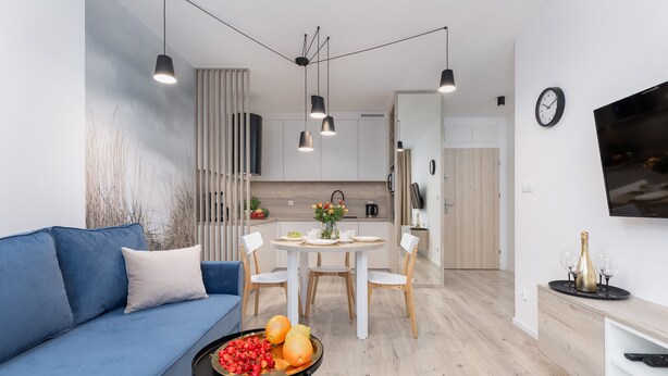 A modern living room with a blue sofa, a round dining table with chairs, and a kitchen area in the background.