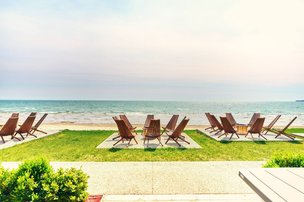 A beachside seating area with lounge chairs and a fire pit, overlooking the ocean.