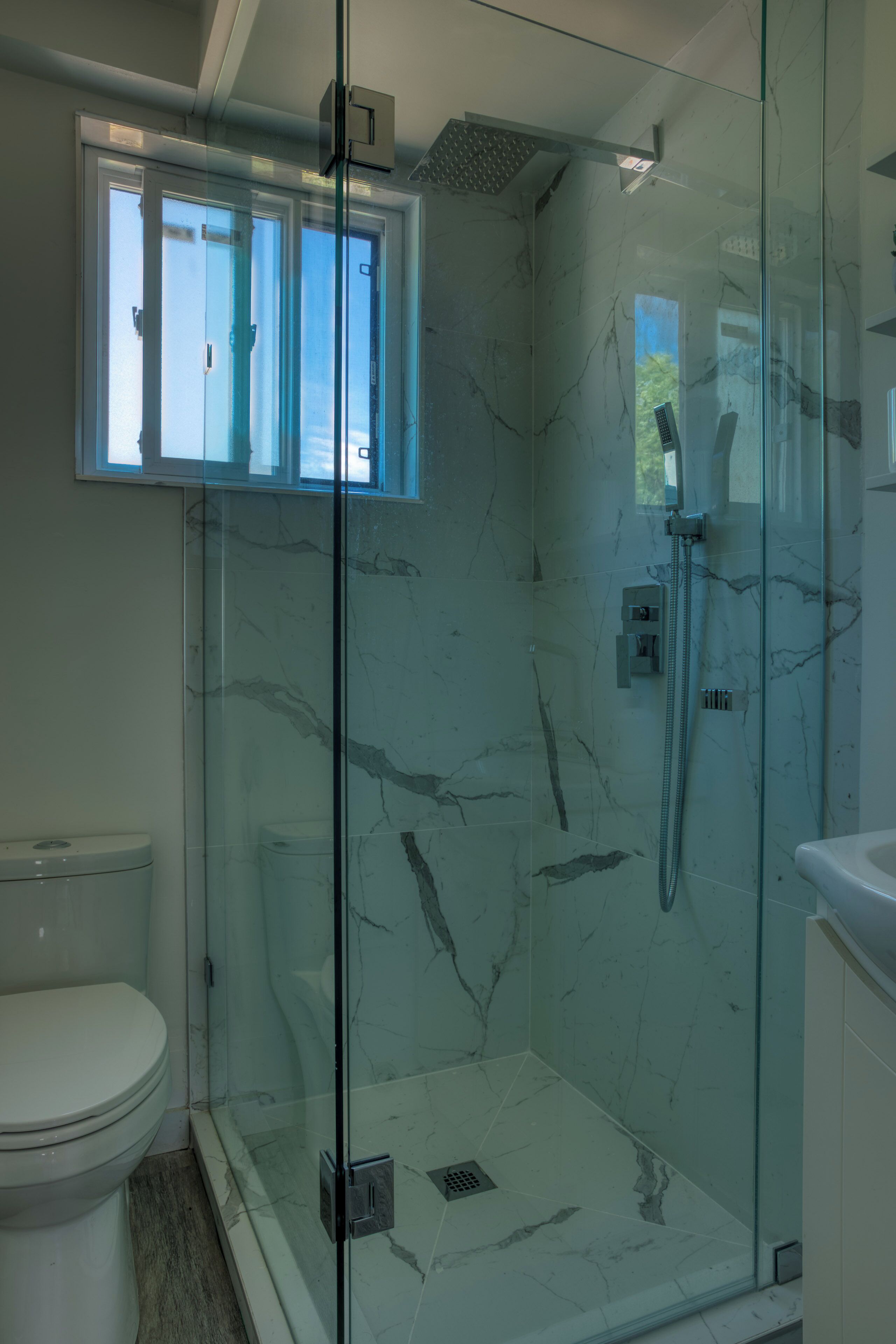 A glass-enclosed shower with a handheld showerhead and a handheld faucet.