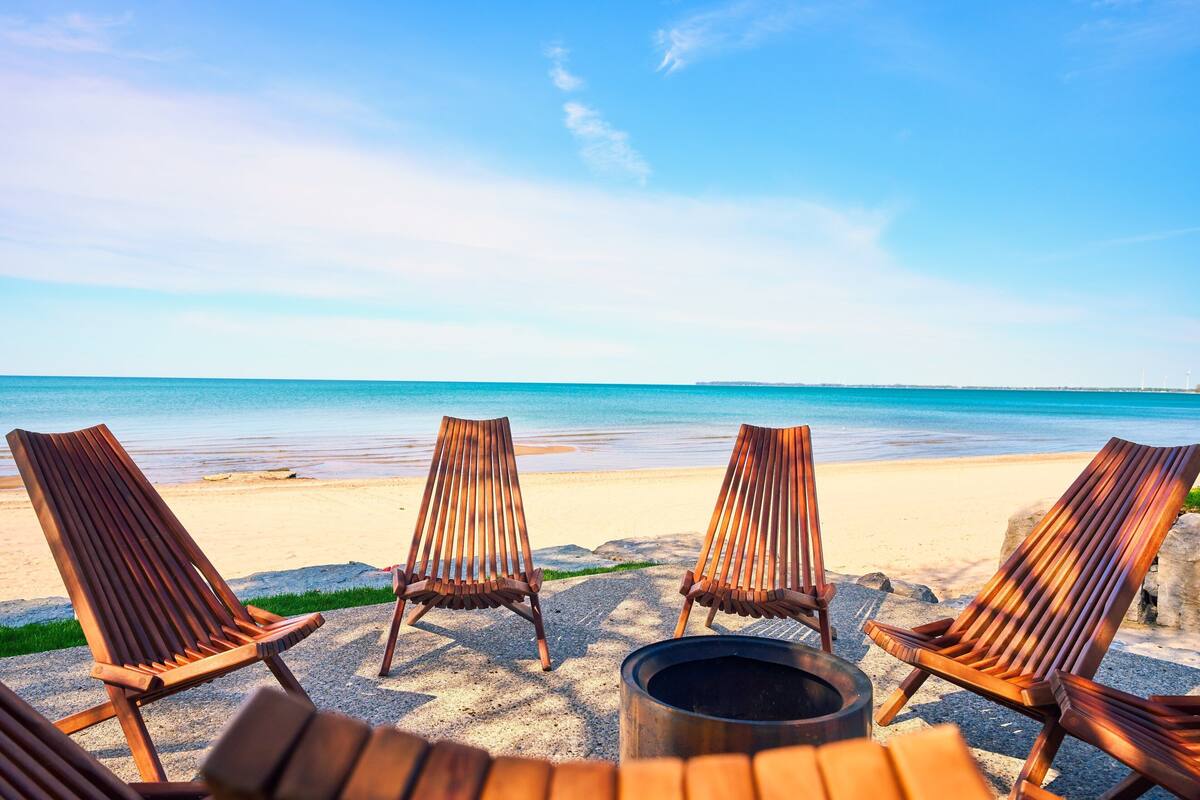 Four wooden lounge chairs arranged on a sandy beach with a clear view of the ocean.