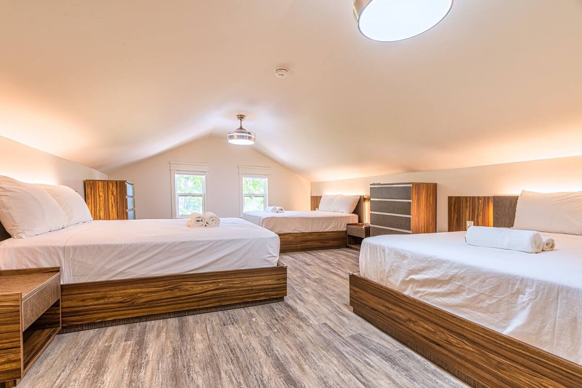 A hotel room with three beds, wooden headboards, and a sloped ceiling with a skylight.