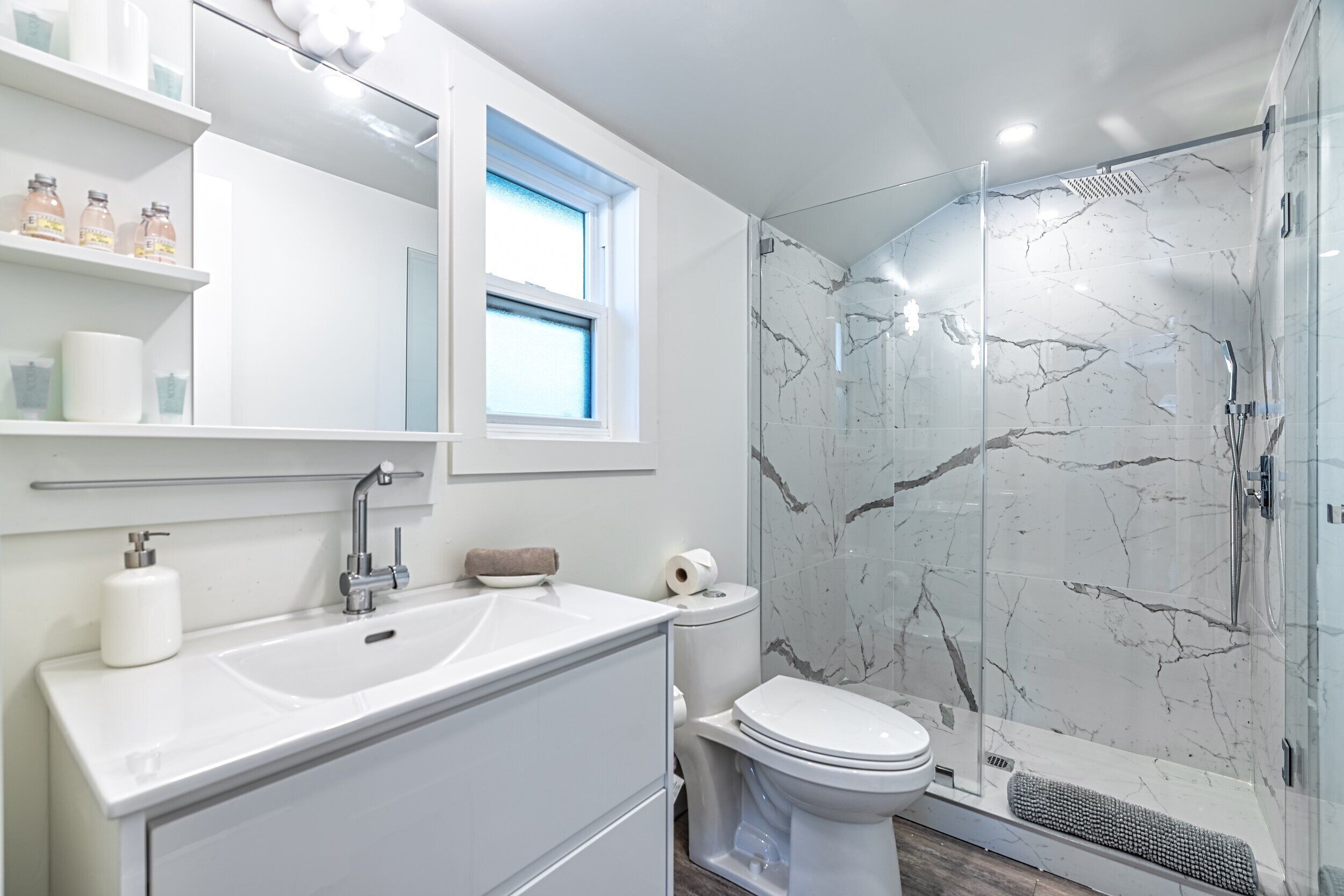 Een moderne badkamer met een witte wastafel, een douchecabine met glazen wanden en een marmeren spatwand.
