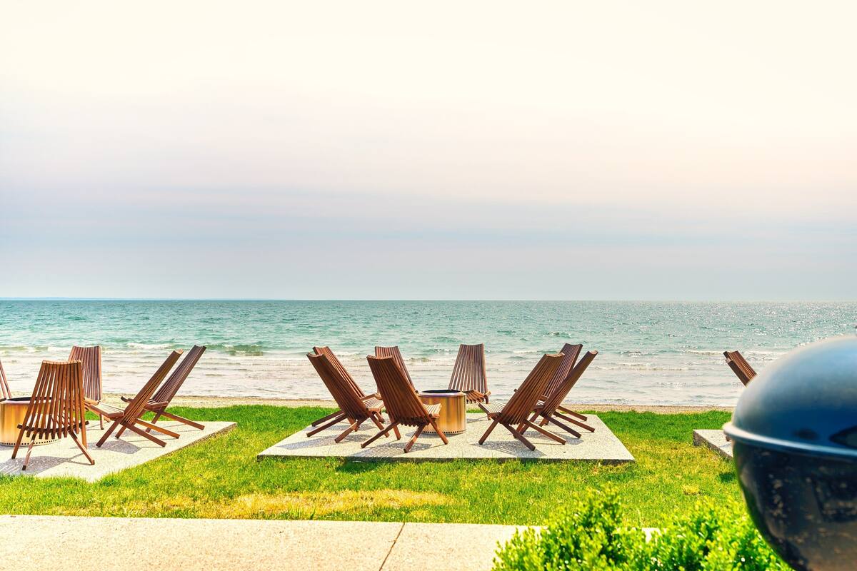 A beachside lounge with wooden chairs and a fire pit, overlooking the ocean.