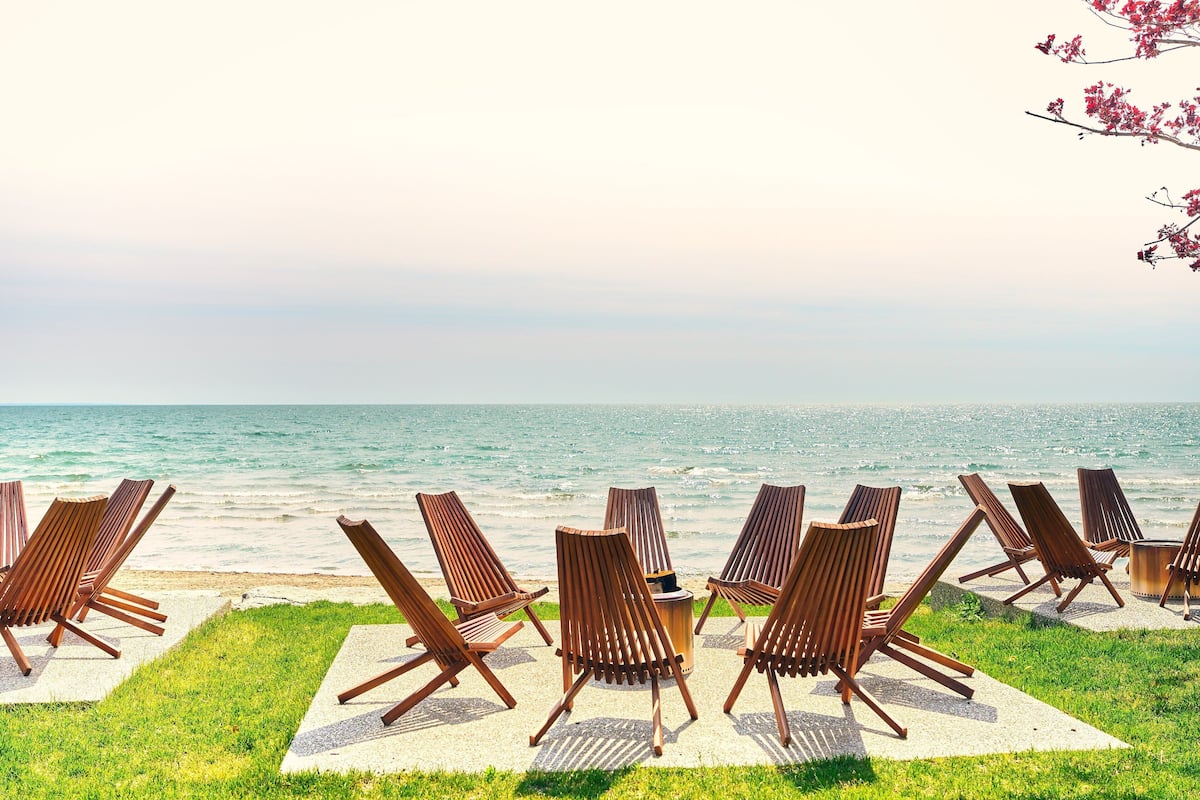 A beachside seating area with wooden chairs and a round table, overlooking the ocean.