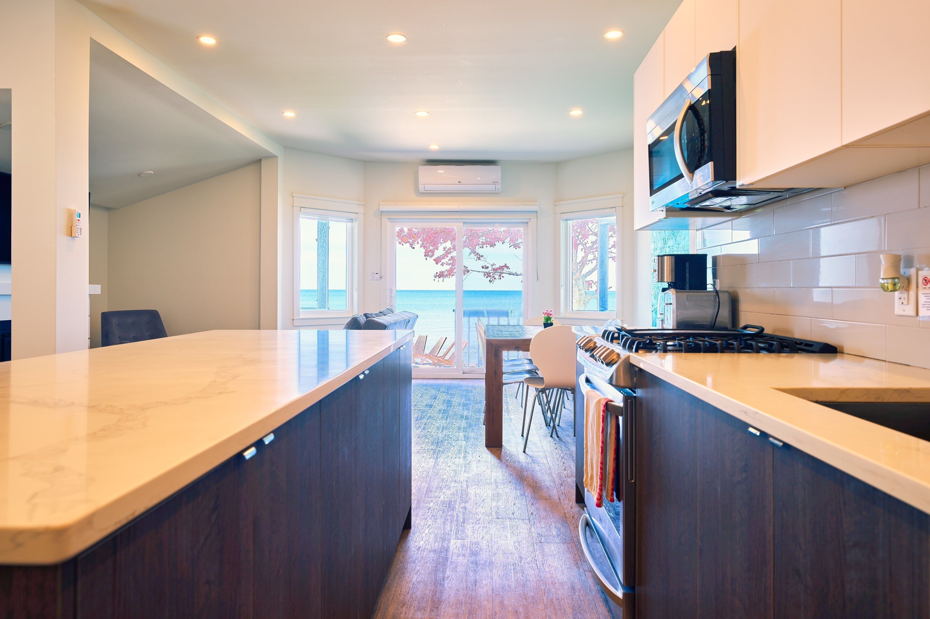 A modern kitchen with dark wood cabinets, a marble countertop, and a view of the sea through large windows.