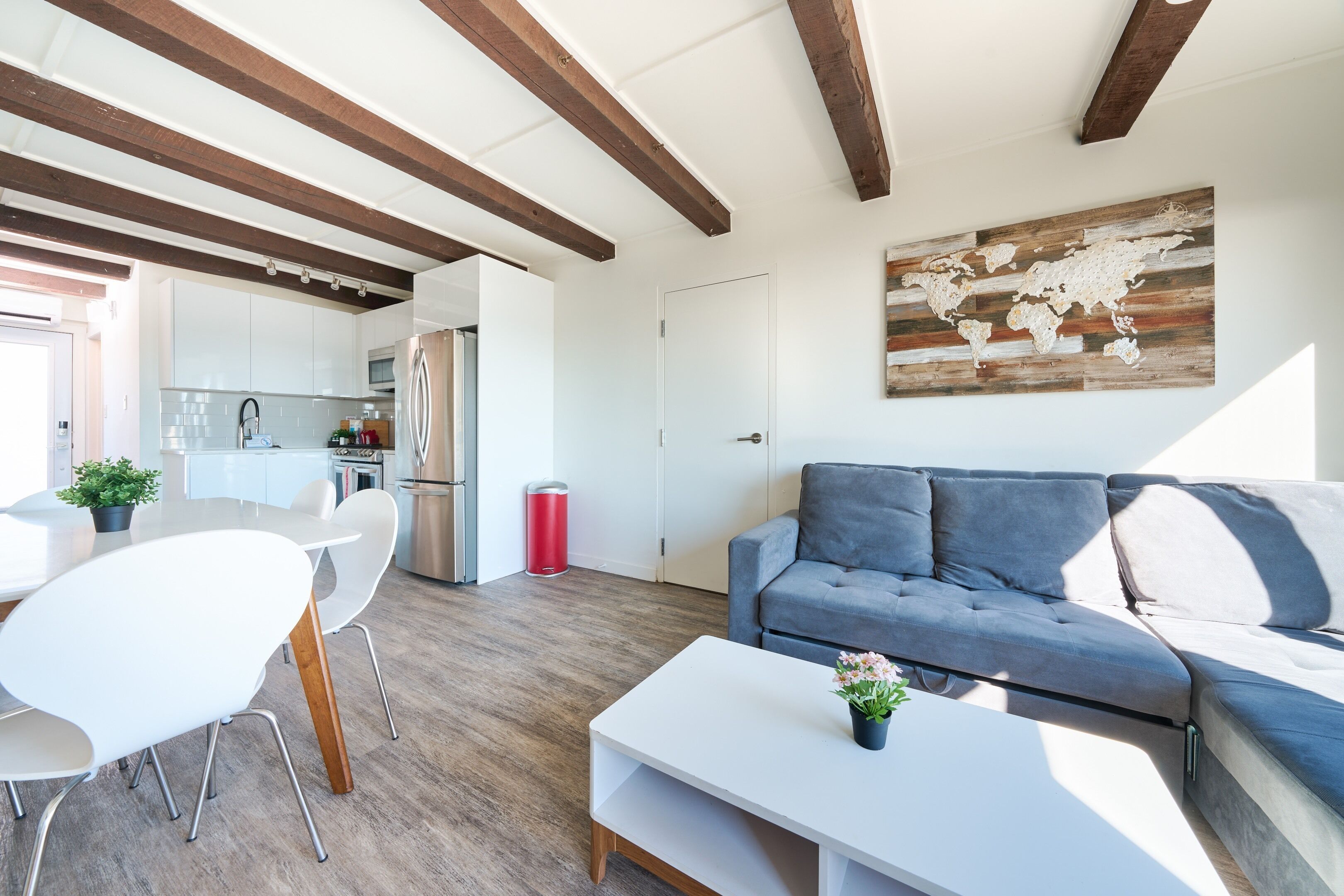 A modern living room with a grey sofa, white coffee table, and white chairs. There is a kitchen in the background with white cabinets and stainless steel appliances.