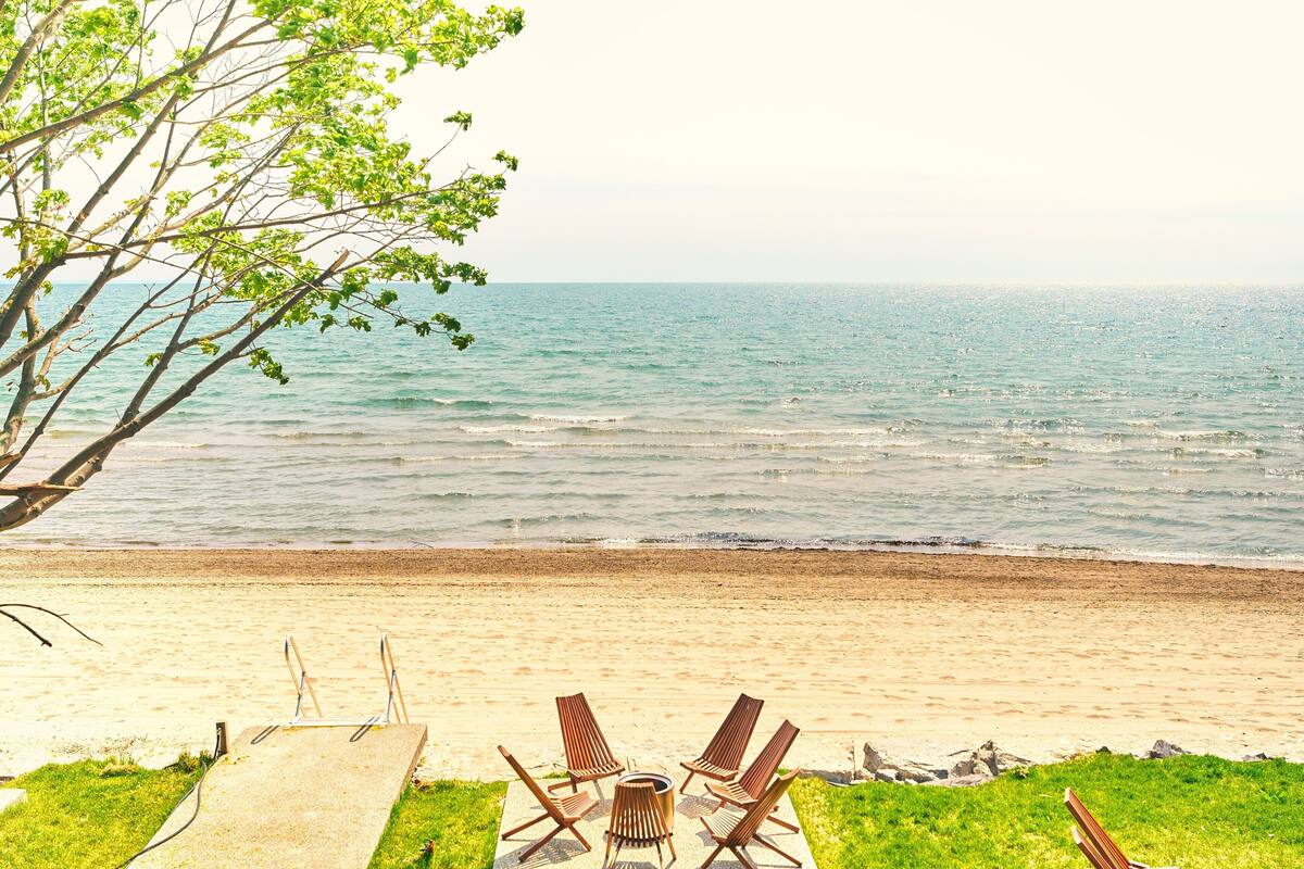 A beach with a concrete deck, four wooden lounge chairs, and a table.