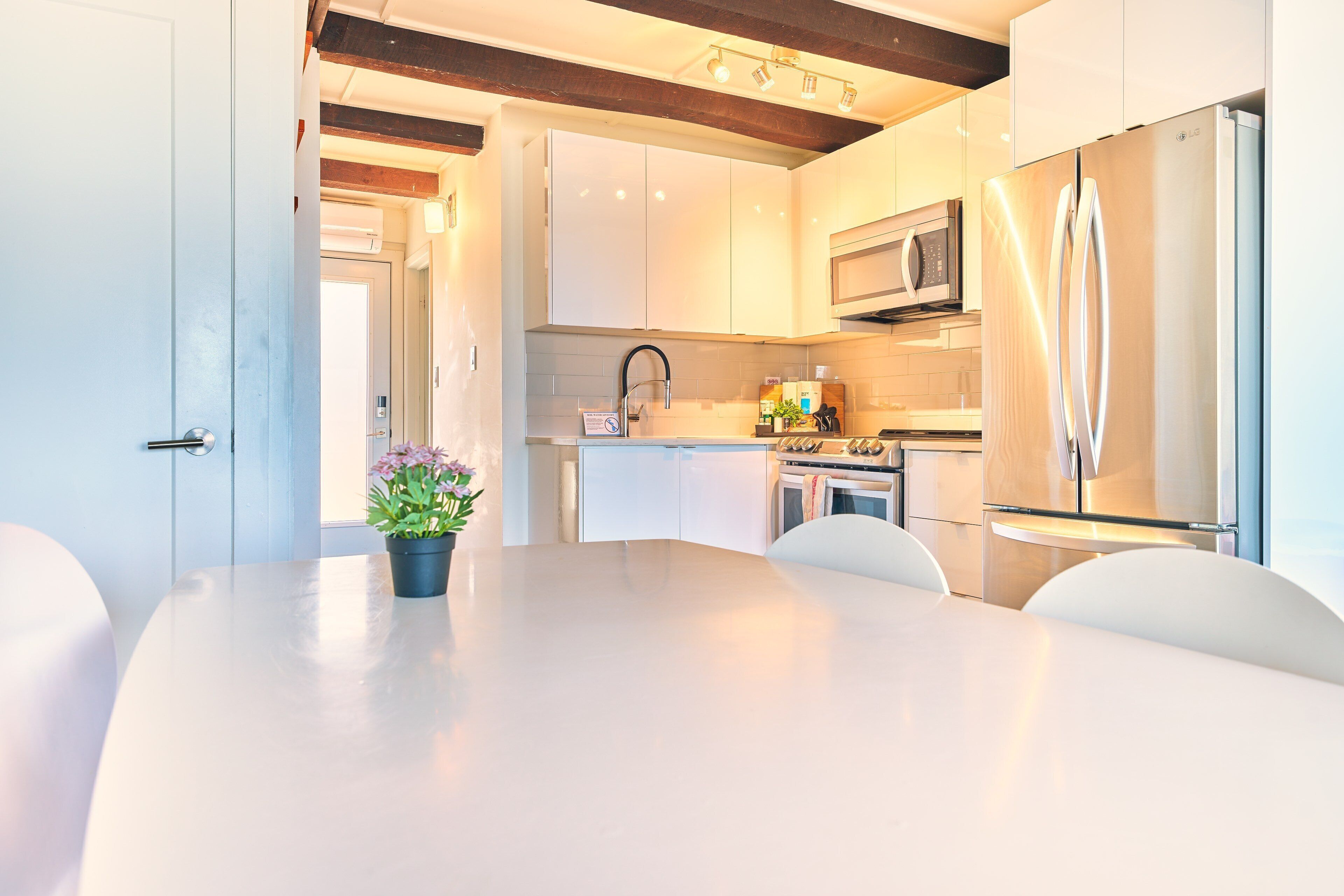 Een moderne keuken met witte kasten, een roestvrijstalen koelkast en een eethoek met een witte tafel en stoelen.