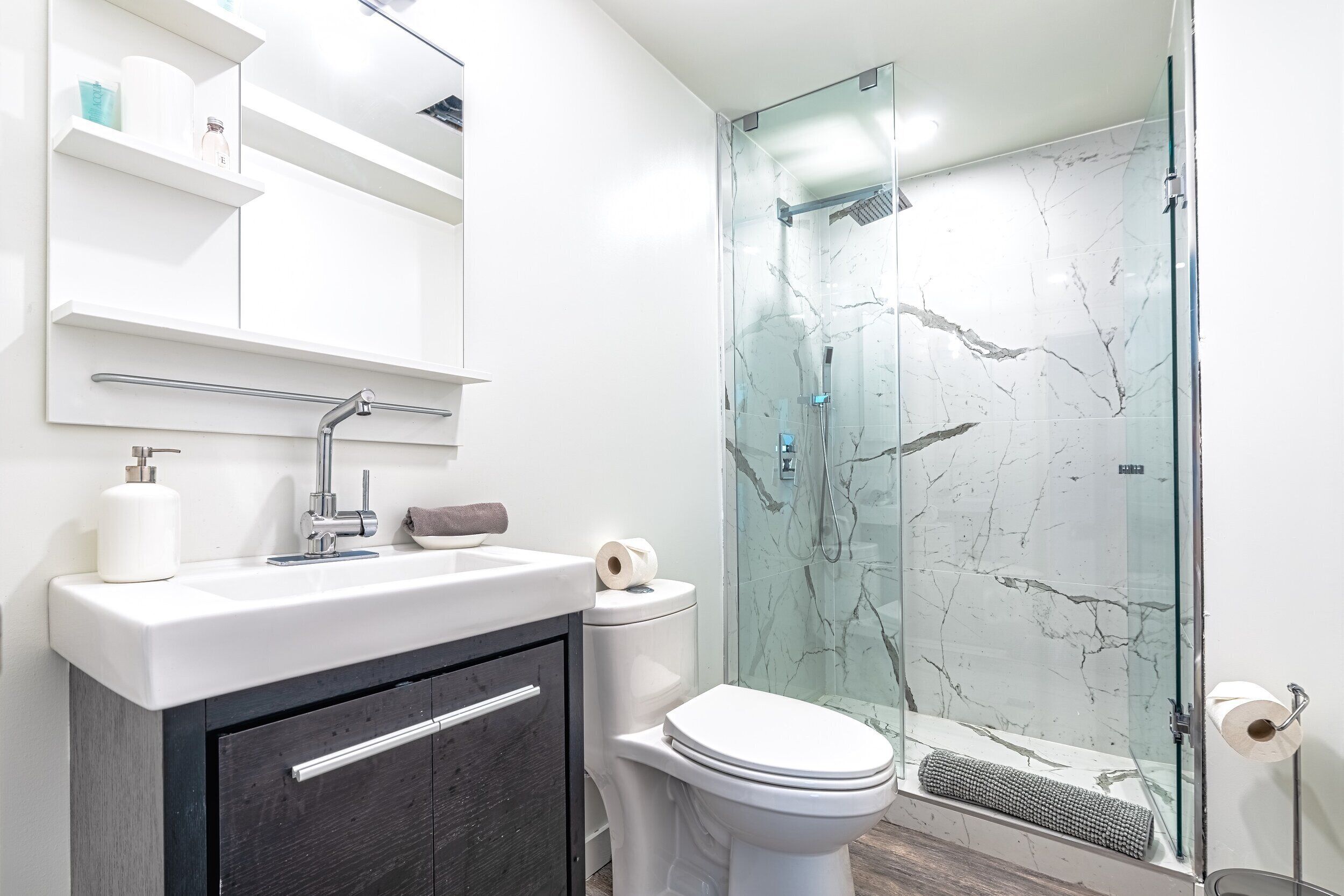 A modern bathroom with a glass-enclosed shower, a white sink, and a dark wooden cabinet.