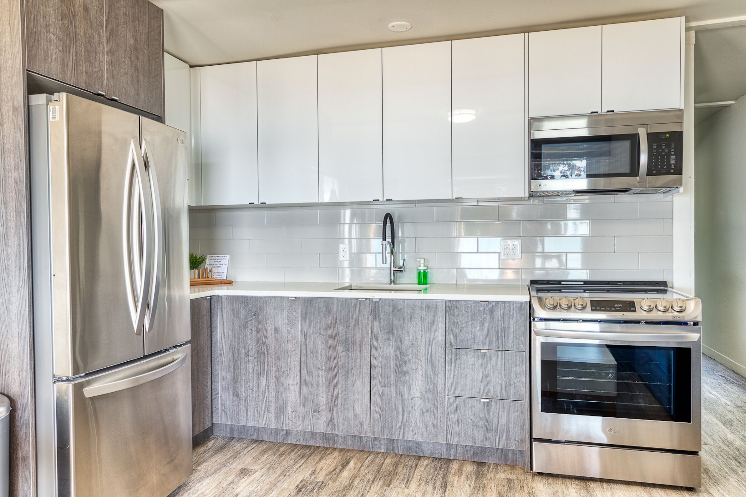 A modern kitchen with stainless steel appliances, grey cabinetry, and a tiled backsplash.