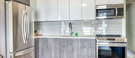 A modern kitchen with stainless steel appliances, grey cabinetry, and a tiled backsplash.
