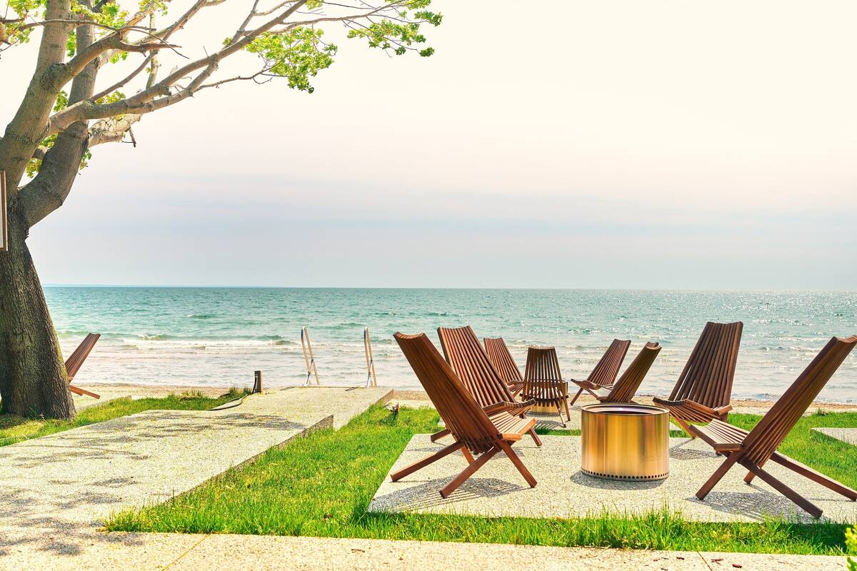 A beachside seating area with wooden chairs and a metal fire pit, overlooking the ocean.