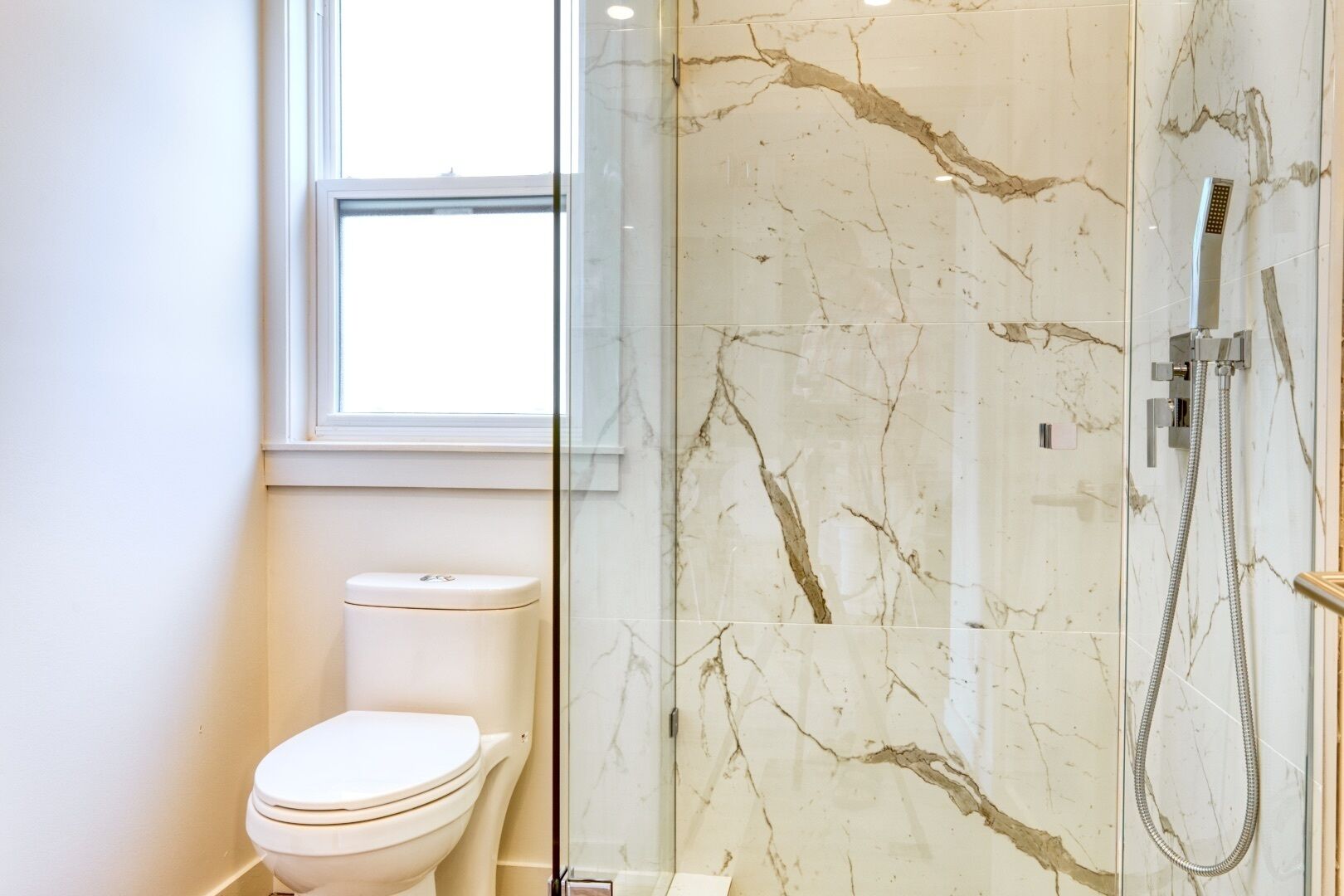 Une salle de bain avec des toilettes, une douche à parois de verre et une fenêtre.