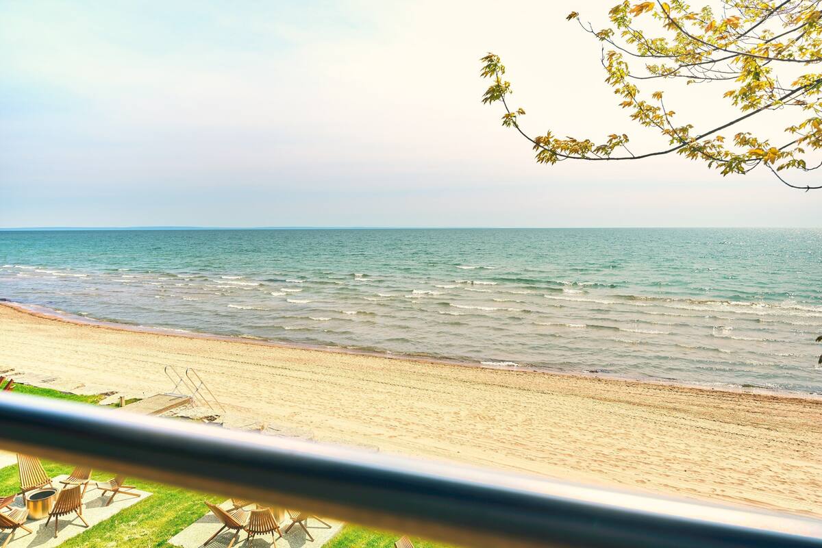 A beach with a view of the ocean, a sandy shore, and some lounge chairs.