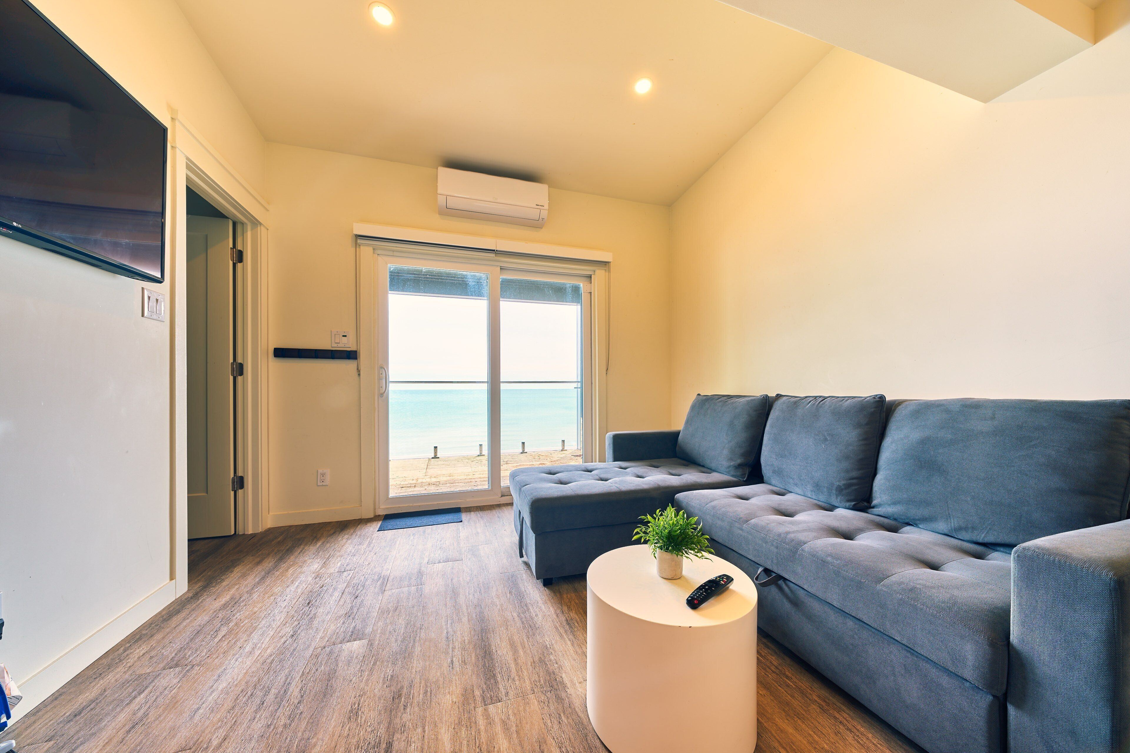 Un salón moderno con un sofá gris, una mesa redonda blanca y vista a la playa a través de un ventanal.