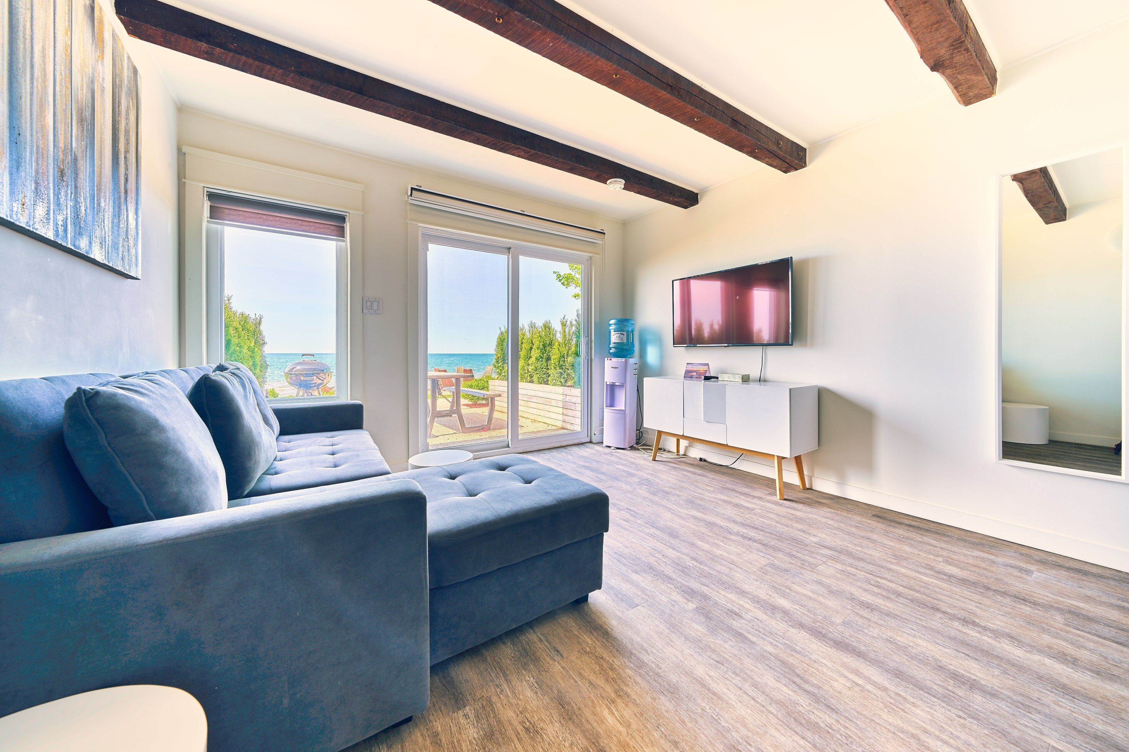 A modern living room with a grey sofa, a flat-screen TV, and a sliding glass door leading to an outdoor patio.