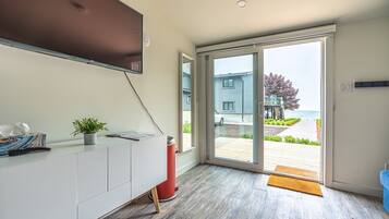 Una habitación moderna con un amplio ventanal corredera que da a un espacio exterior, un armario blanco con una planta y un televisor de pantalla plana montado en la pared.