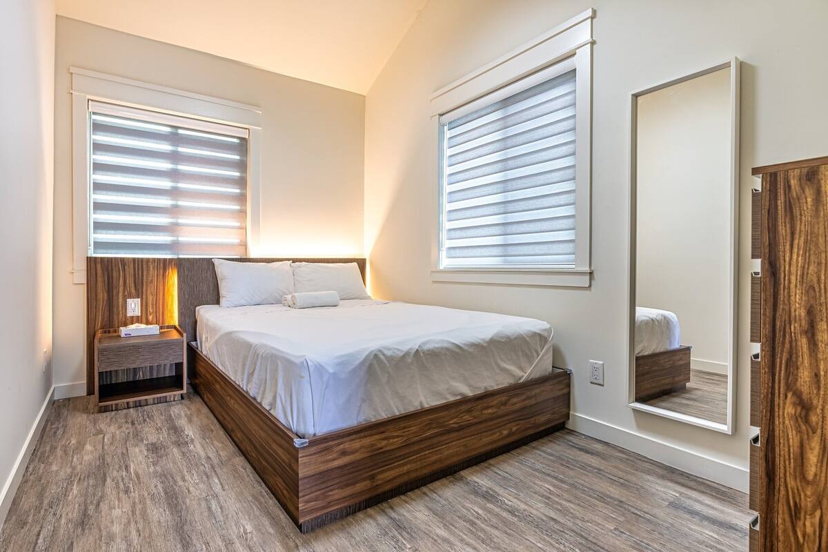 A bedroom with a wooden bed frame, two bedside tables, a nightstand, and a large mirror.