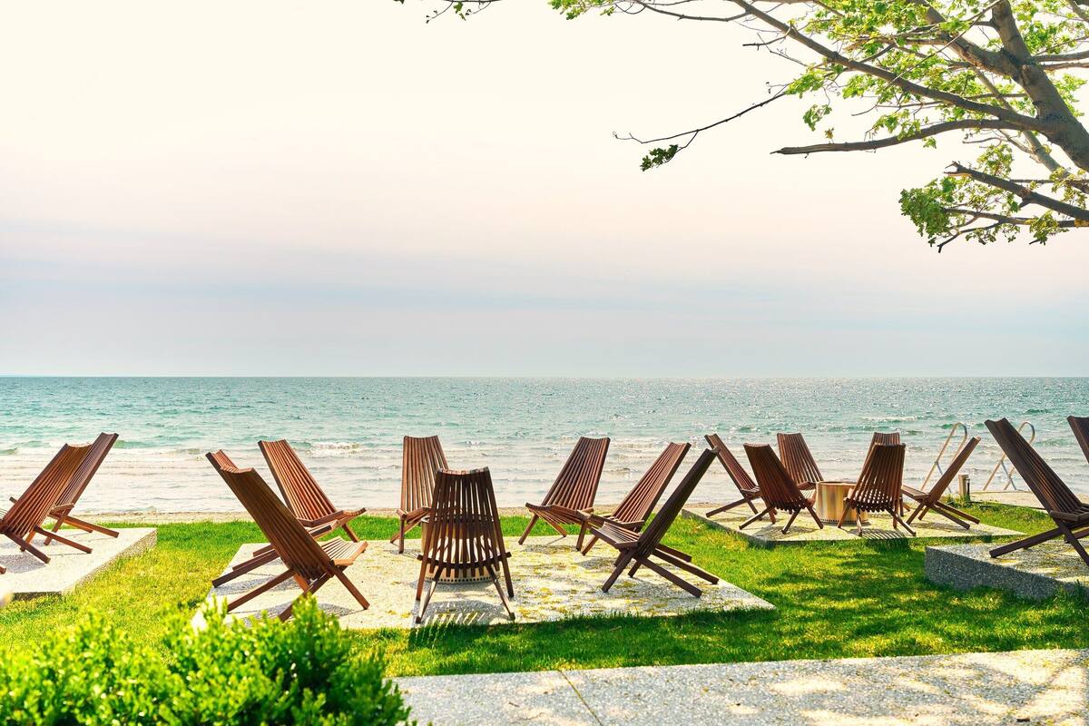 A row of wooden lounge chairs facing a beach with a clear view of the ocean.