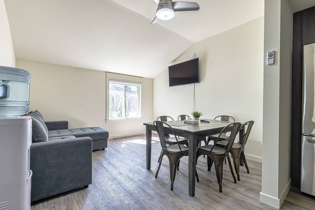 A compact living space with a dining area, a grey sofa, a flat-screen TV, and a ceiling fan.