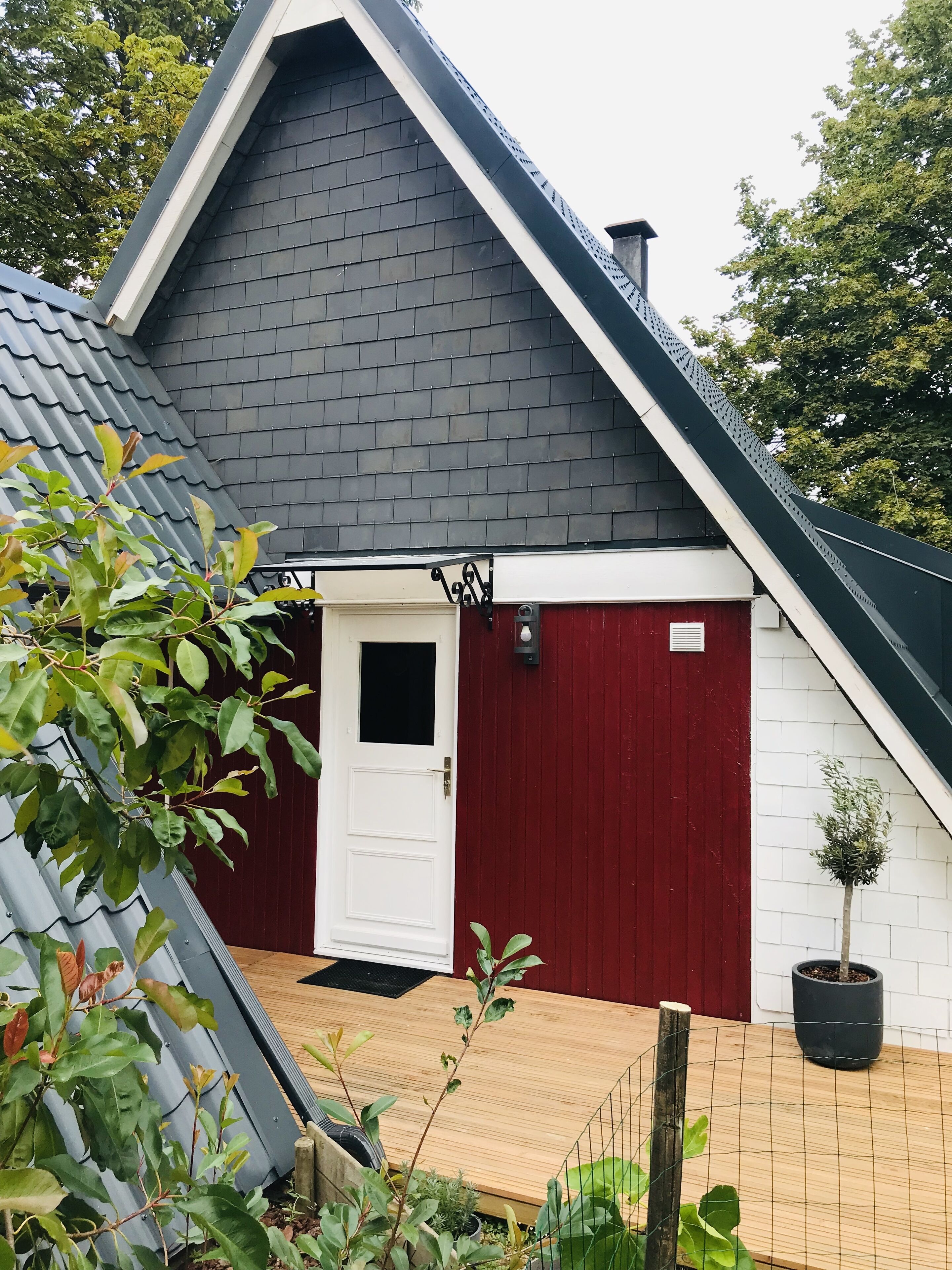 Una casa con una porta rossa, un muro esterno bianco e un tetto grigio.