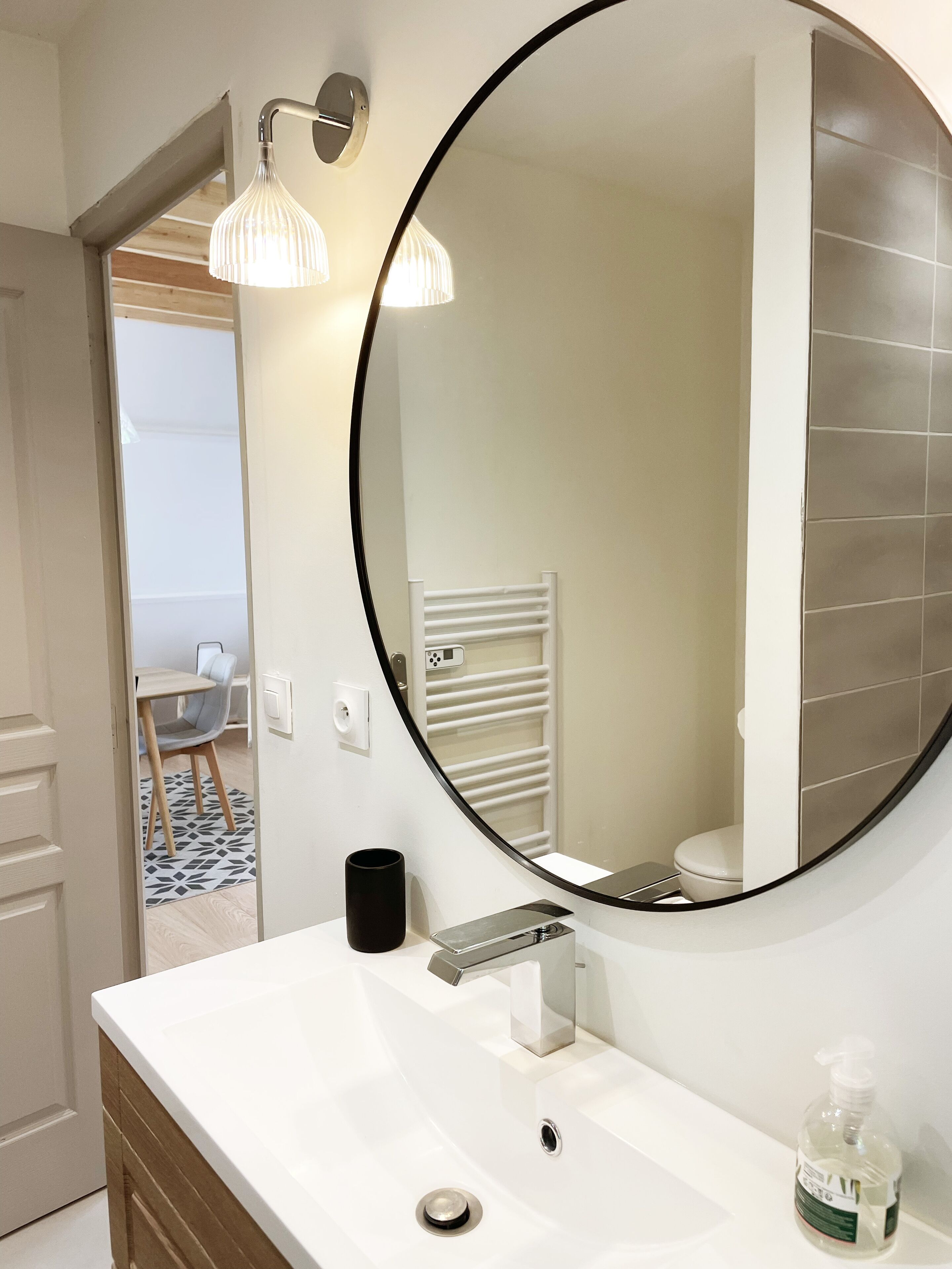 A bathroom with a round mirror, white sink, and a towel rack.