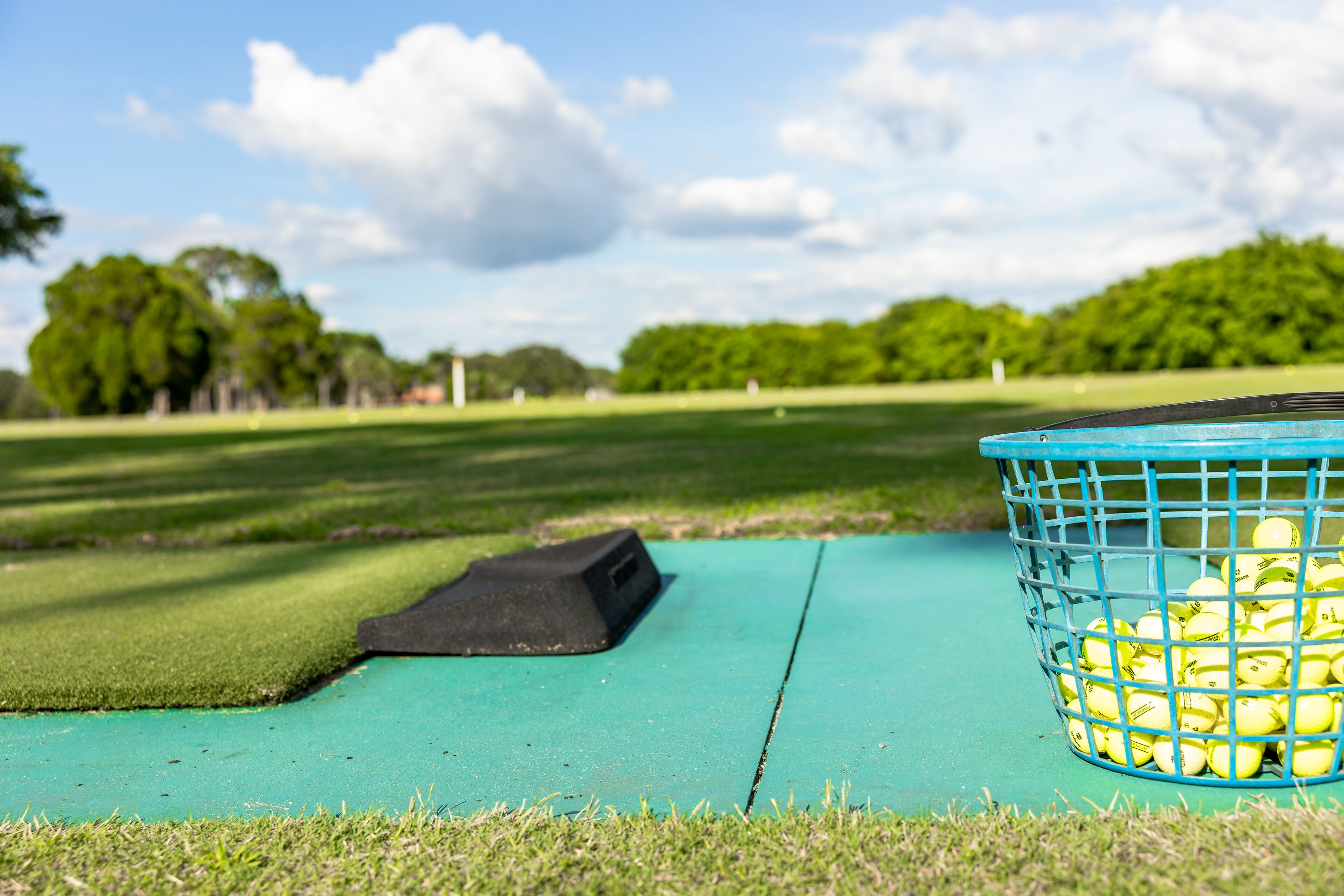 Uma mala de golfe e bolas em um tapete verde em um parque.