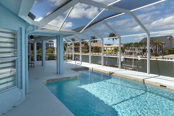 A pool area with a covered deck, clear pool water, and a view of the surrounding neighborhood. - Nice House with Water View and Private Pool (Marco Island)